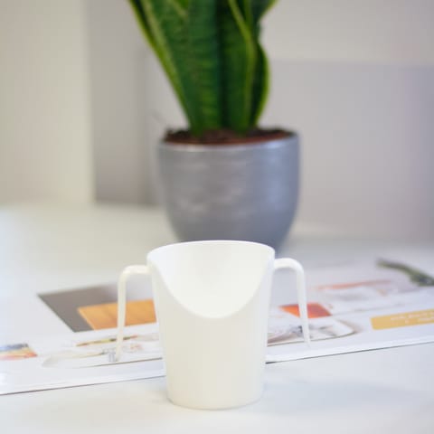 A white nose cup with 2 handles on a table.